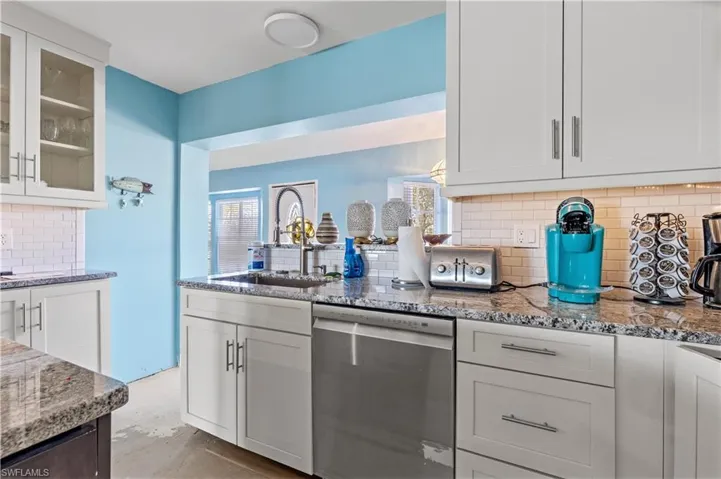 Kitchen featuring dishwasher, white cabinetry, light stone countertops, and sink