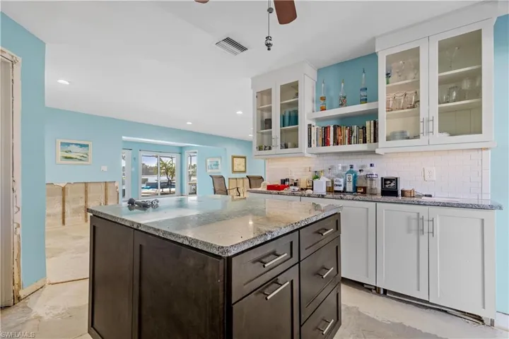 Kitchen with decorative backsplash, light stone countertops, dark brown cabinets, and white cabinets