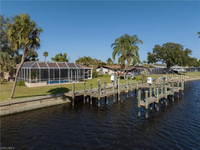 View of dock with a water view, glass enclosure, and a lawn