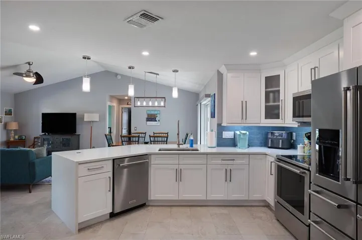 Kitchen with white cabinets, appliances with stainless steel finishes, decorative light fixtures, and sink