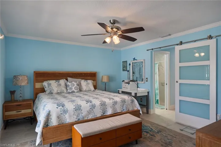 Bedroom featuring a barn door to the bath, ceiling fan, crown molding