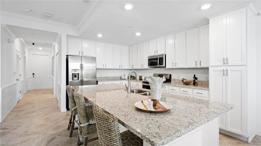 Kitchen with light stone counters, appliances with stainless steel finishes, and an island with sink