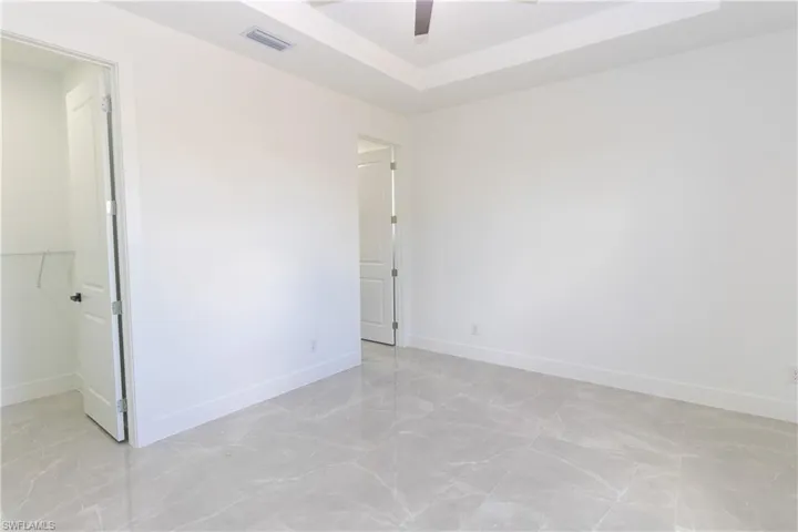 Unfurnished bedroom featuring a tray ceiling, a walk in closet, ceiling fan, and light marble finish floors