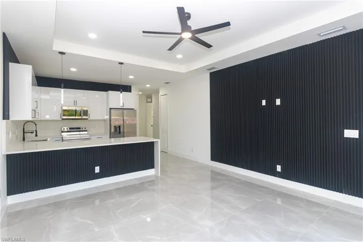 Kitchen featuring white cabinetry, stainless steel appliances, a raised ceiling, modern cabinets, and light stone counters