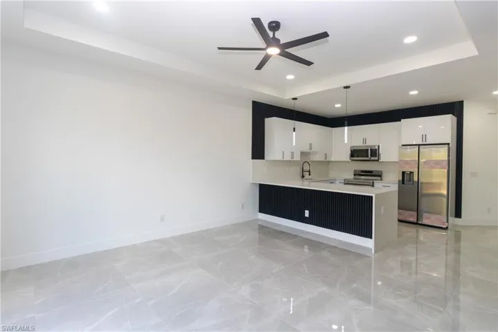 Kitchen featuring a raised ceiling, stainless steel appliances, a peninsula, white cabinetry, and light stone counters