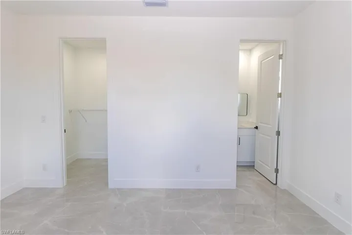 Unfurnished bedroom featuring a walk in closet, light marble finish floors, and connected bathroom