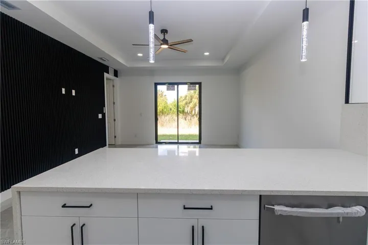Kitchen with light stone countertops, white cabinets, a ceiling fan, pendant lighting, and open floor plan
