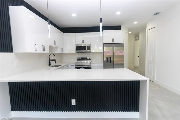 Kitchen with decorative light fixtures, stainless steel appliances, a peninsula, white cabinetry, and light stone countertops