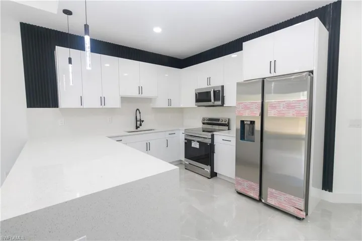 Kitchen with stainless steel appliances, hanging light fixtures, white cabinets, and light stone counters