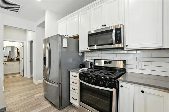 Kitchen with stainless steel appliances, white cabinetry, tasteful backsplash, and light wood-style flooring