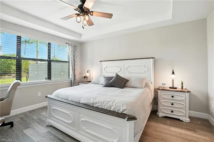 Bedroom featuring a tray ceiling, light wood-style flooring, ceiling fan, and a desk
