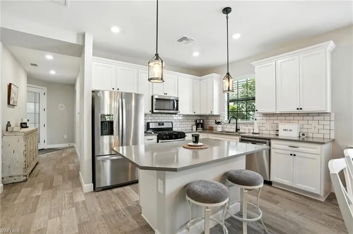 Kitchen with stainless steel appliances, a kitchen island, light wood-type flooring, white cabinets, and a breakfast bar