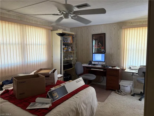 Office with ceiling fan, carpet, and wood walls