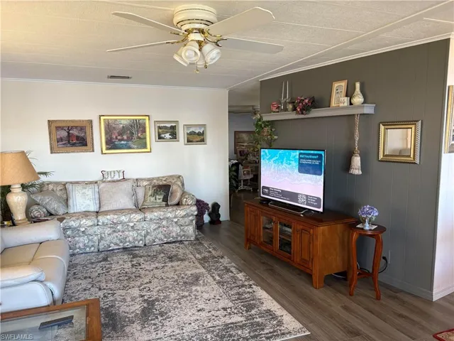 Living room with wooden walls, ceiling fan, ornamental molding, and hardwood / wood-style flooring