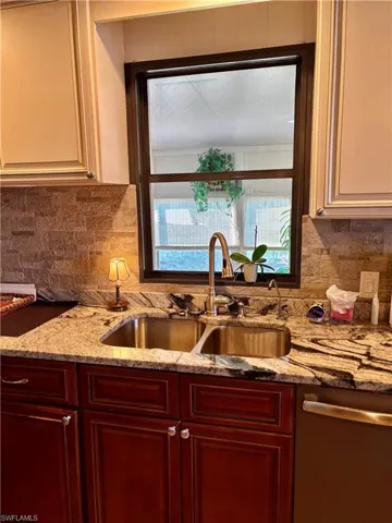 Kitchen with decorative backsplash, dishwasher, sink, and light stone counters