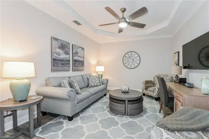 Living room with a tray ceiling, crown molding, ceiling fan, and light wood-style flooring