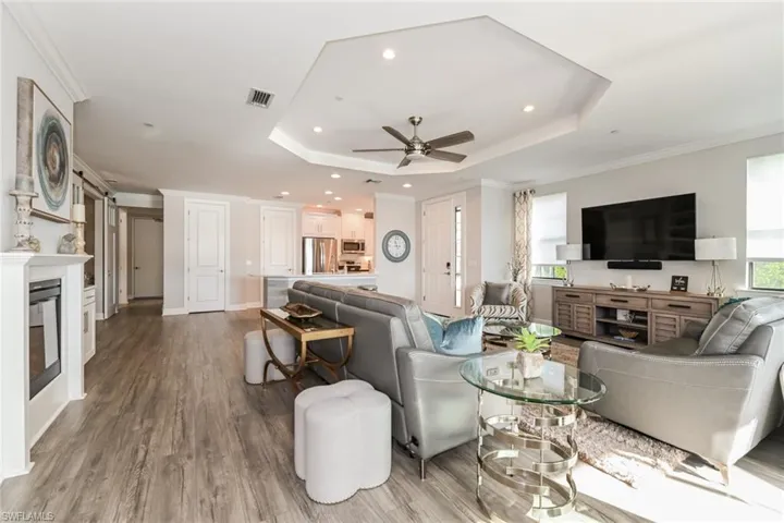 Living room featuring a raised ceiling, ornamental molding, a ceiling fan, wood finished floors, and a glass covered fireplace