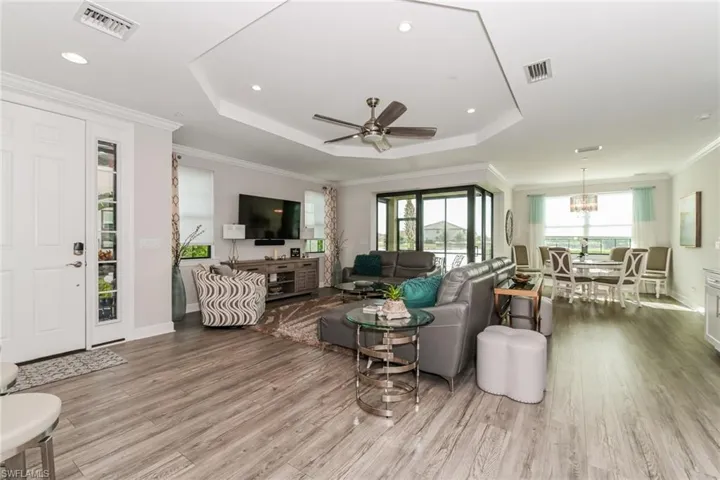 Living room featuring a tray ceiling, ornamental molding, a ceiling fan, light wood-type flooring, and recessed lighting