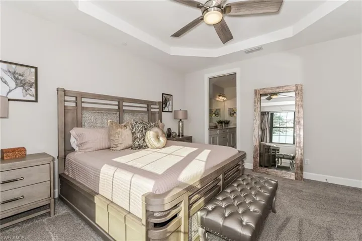 Carpeted bedroom featuring a raised ceiling, a ceiling fan, and ensuite bathroom