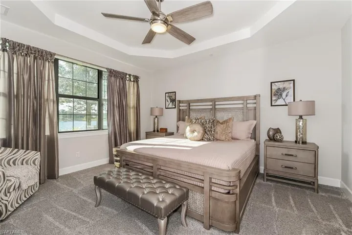 Carpeted bedroom with a tray ceiling and a ceiling fan