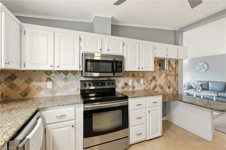 Kitchen featuring appliances with stainless steel finishes, tasteful backsplash, light stone counters, white cabinetry, and lofted ceiling