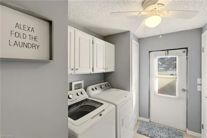 Laundry area with a ceiling fan, washer and dryer, cabinet space, and a textured ceiling