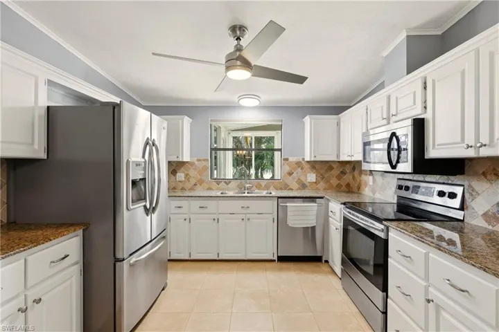 Kitchen with stainless steel appliances, white cabinets, dark stone counters, and crown molding