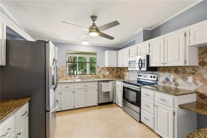 Kitchen with appliances with stainless steel finishes, dark stone countertops, white cabinets, ornamental molding, and light tile patterned flooring