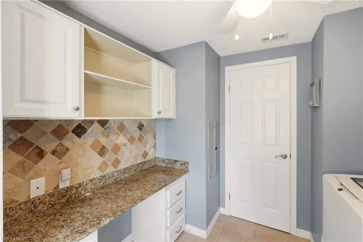 Kitchen with tasteful backsplash, built in desk, light stone countertops, open shelves, and white cabinetry