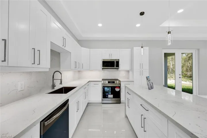 Kitchen with stainless steel appliances, a raised ceiling, light stone counters, hanging light fixtures, and sink