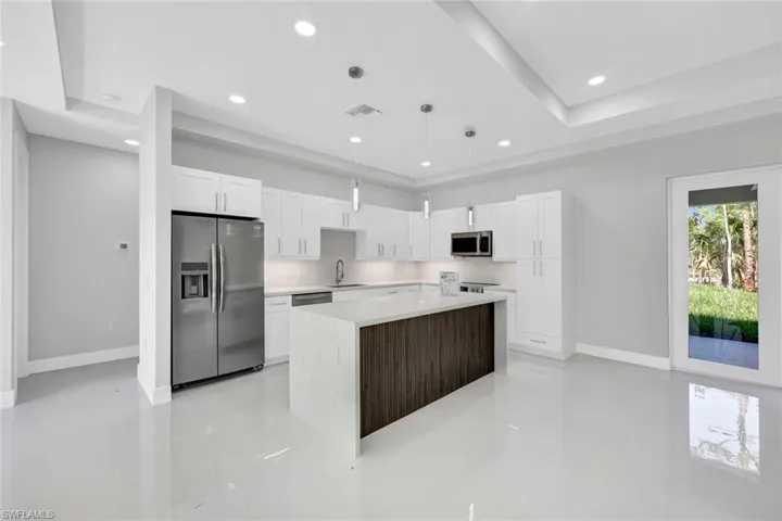 Kitchen with stainless steel appliances, a raised ceiling, hanging light fixtures, a center island, and sink