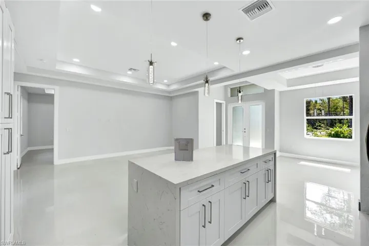 Kitchen with hanging light fixtures, white cabinets, light stone countertops, and a center island