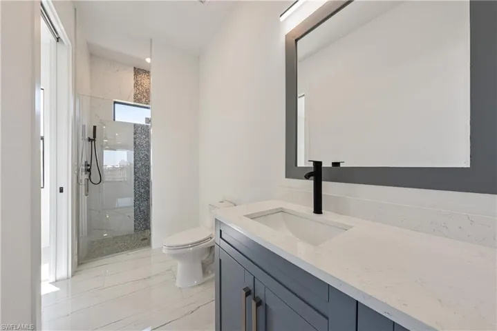 Bathroom with vanity, toilet, marble finish floor, and a marble finish shower