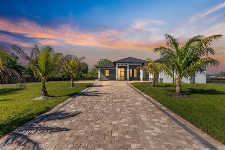 View of front of property with decorative driveway, a yard, and fence