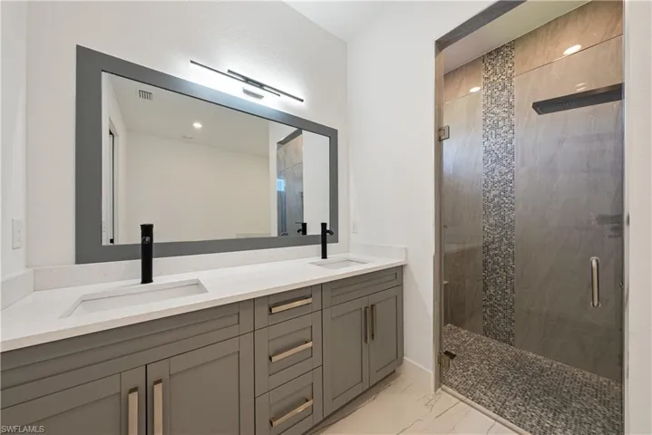 Full bathroom with double vanity, marble finish floor, a shower stall, and a sink