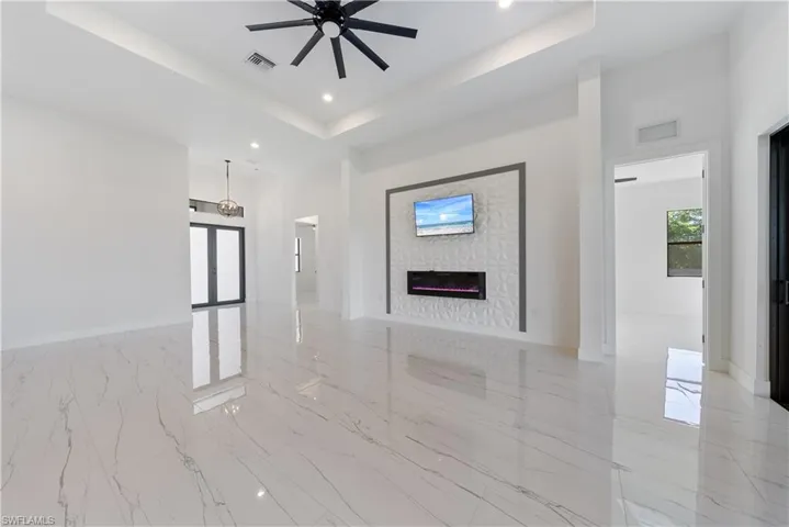 Unfurnished living room with a tray ceiling, visible vents, marble finish floor, and a ceiling fan