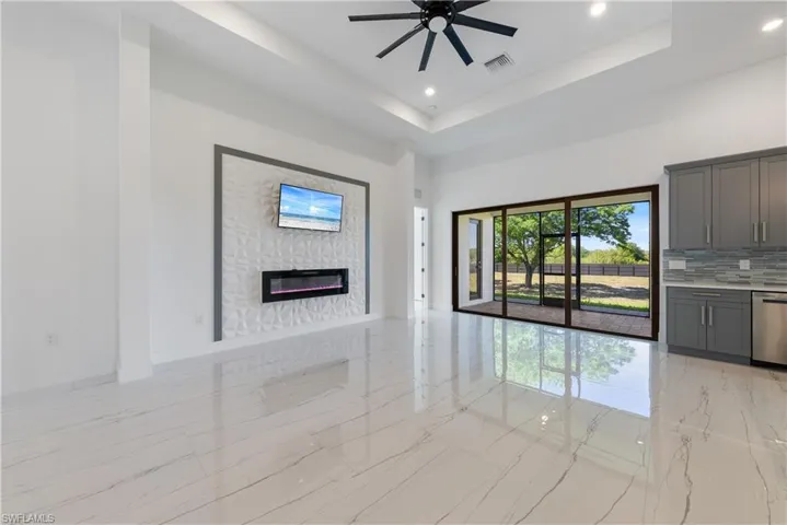 Unfurnished living room featuring a ceiling fan, visible vents, a glass covered fireplace, a raised ceiling, and marble finish floor