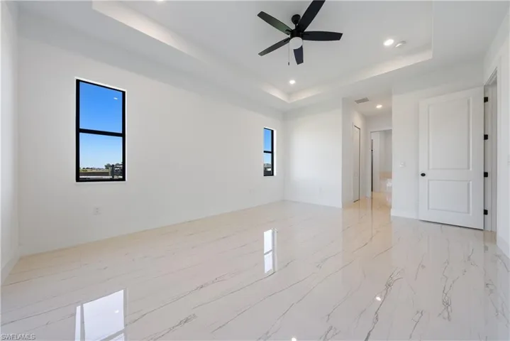 Unfurnished room featuring a tray ceiling, a healthy amount of sunlight, baseboards, and ceiling fan