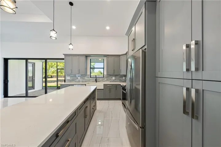 Kitchen with tasteful backsplash, gray cabinetry, pendant lighting, freestanding refrigerator, and marble finish floor