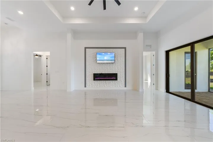 Unfurnished living room featuring a high ceiling, a fireplace, a tray ceiling, and ceiling fan