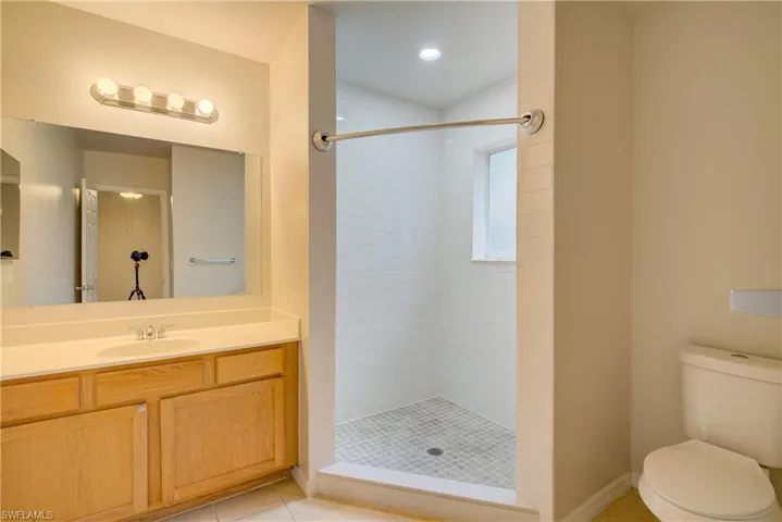 Bathroom featuring vanity, tiled shower, tile patterned floors, and toilet