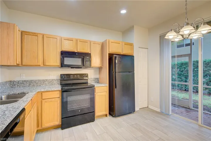 Kitchen with light brown cabinetry, light stone counters, light hardwood / wood-style flooring, pendant lighting, and black appliances