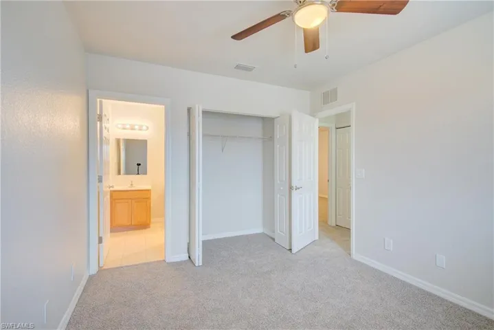 Unfurnished bedroom with ensuite bath, light carpet, ceiling fan, and a closet