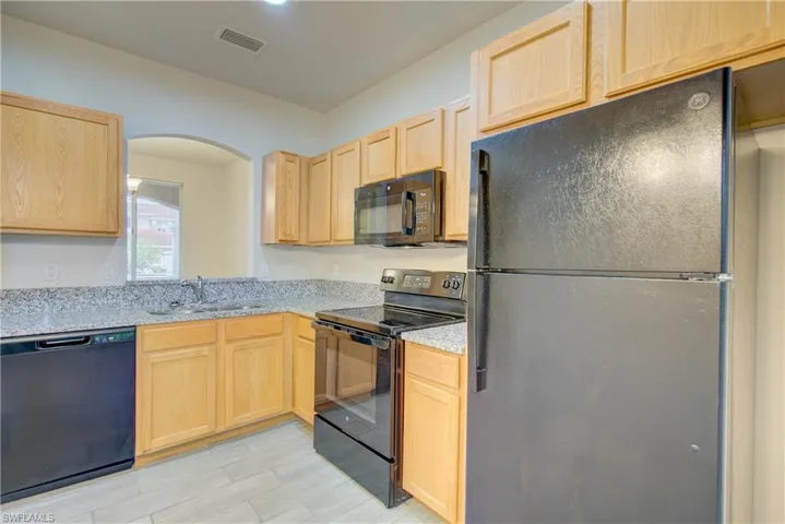Kitchen with light stone countertops, sink, light brown cabinets, and black appliances
