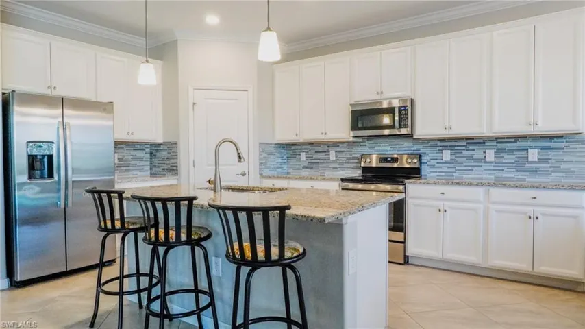 Kitchen featuring stainless steel appliances, a breakfast bar, an island with sink, white cabinetry, and light stone countertops