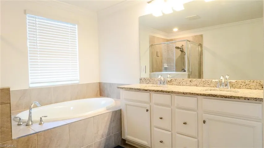 Full bath with double vanity, ornamental molding, a garden tub, and a shower stall