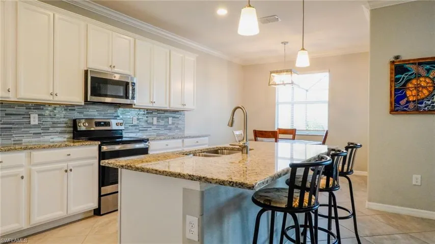 Kitchen featuring stainless steel appliances, a kitchen bar, an island with sink, light stone countertops, and light tile patterned floors