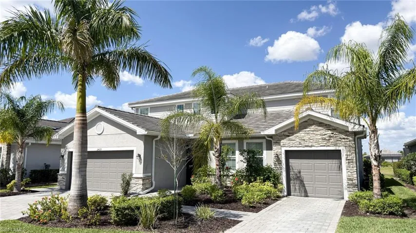 Traditional-style house featuring decorative driveway, stone siding, an attached garage, and stucco siding