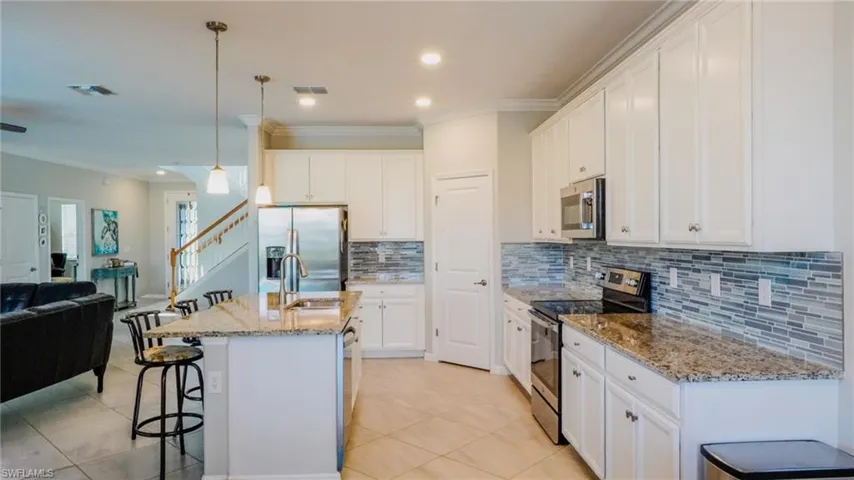 Kitchen featuring stainless steel appliances, open floor plan, a kitchen breakfast bar, white cabinets, and a kitchen island with sink