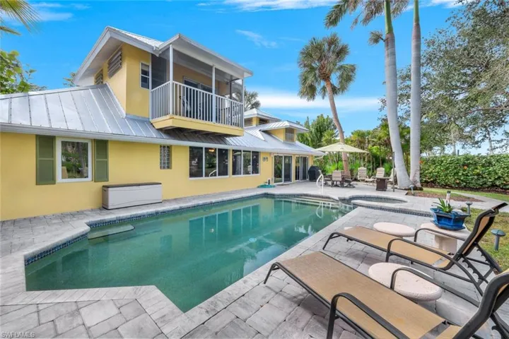 Rear view of house with a balcony, a pool with hot tub, and a patio